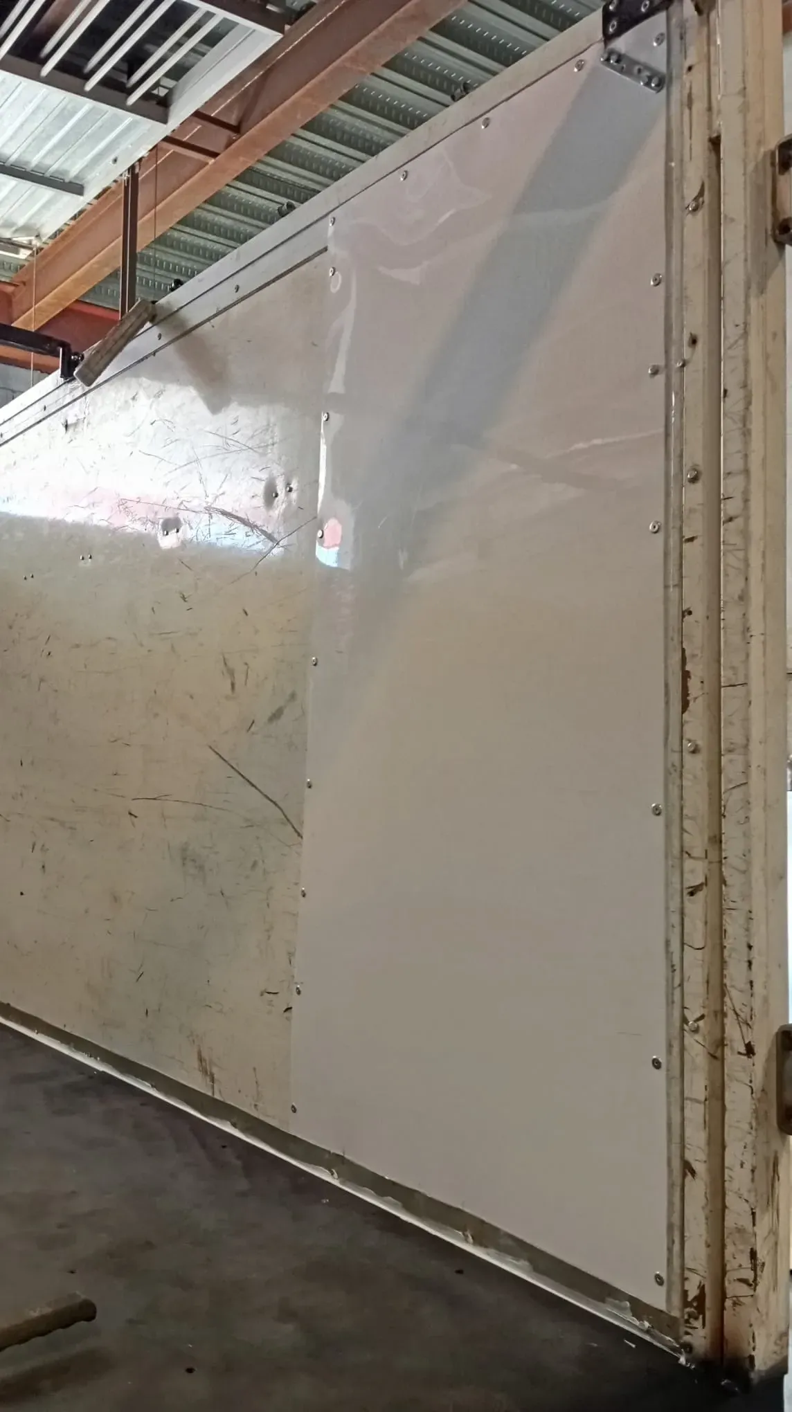 Pared de remolque blanca con estructura de metal remachado en entorno industrial.
