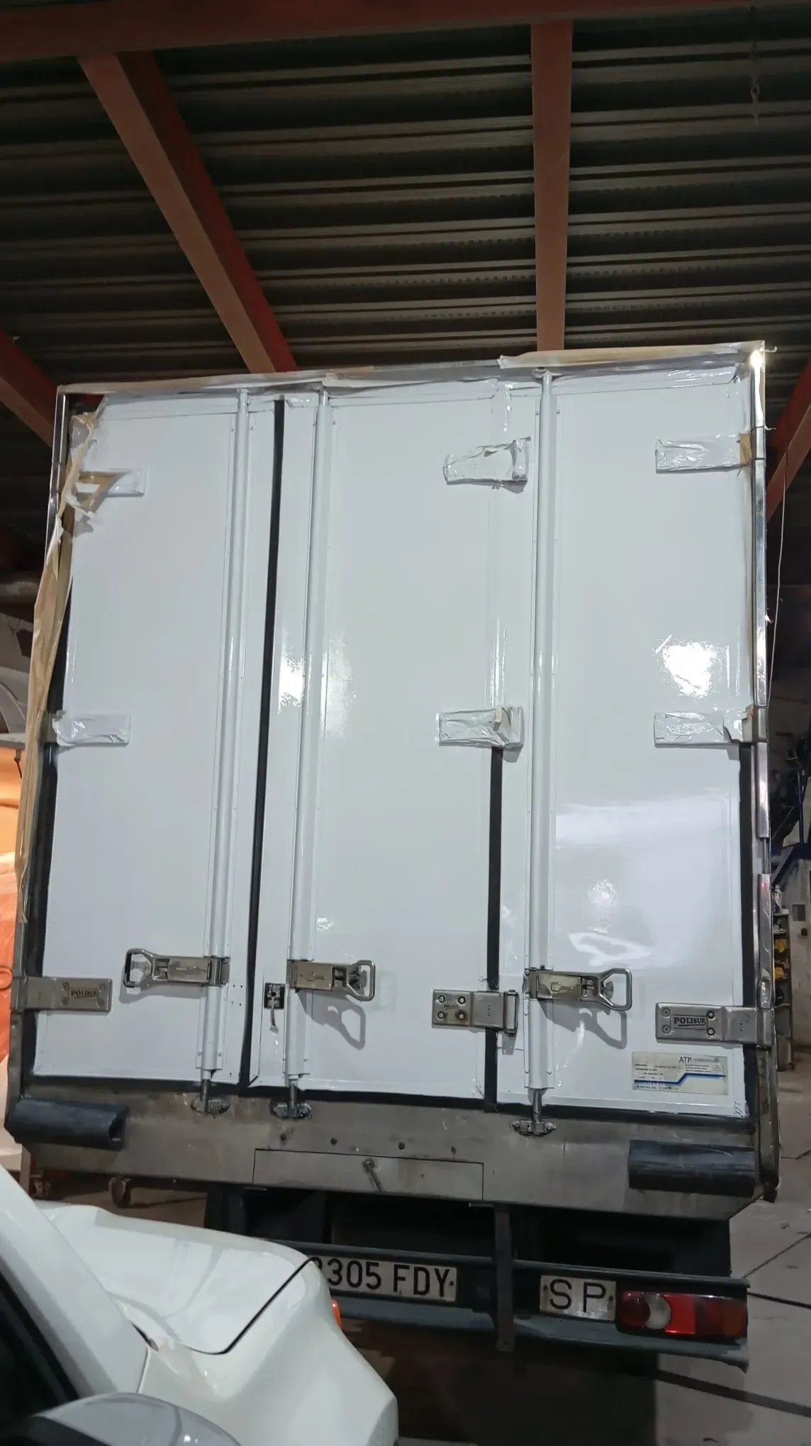 Parte trasera de un camión refrigerado blanco con puertas cerradas bajo el techo de un almacén.