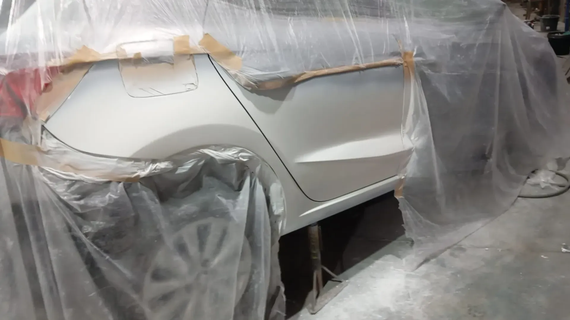 Panel trasero del coche preparándose para pintar. Coche blanco, lona de plástico, cinta de carrocero y decoración interior.