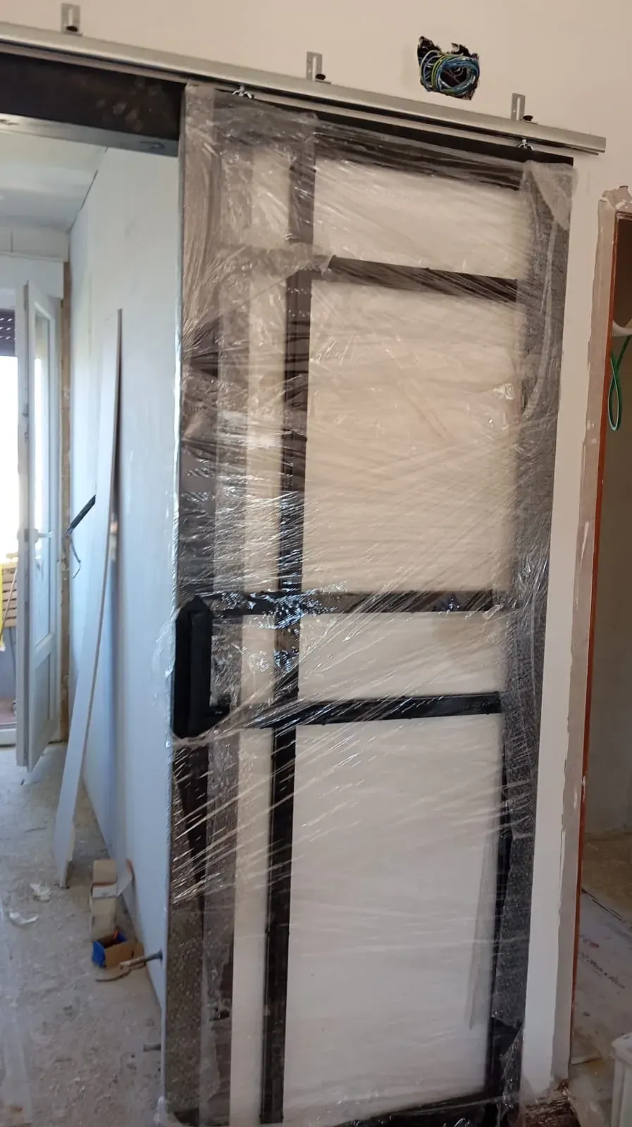 Puerta corrediza recubierta de film plástico, marco metálico, instalada en portal.