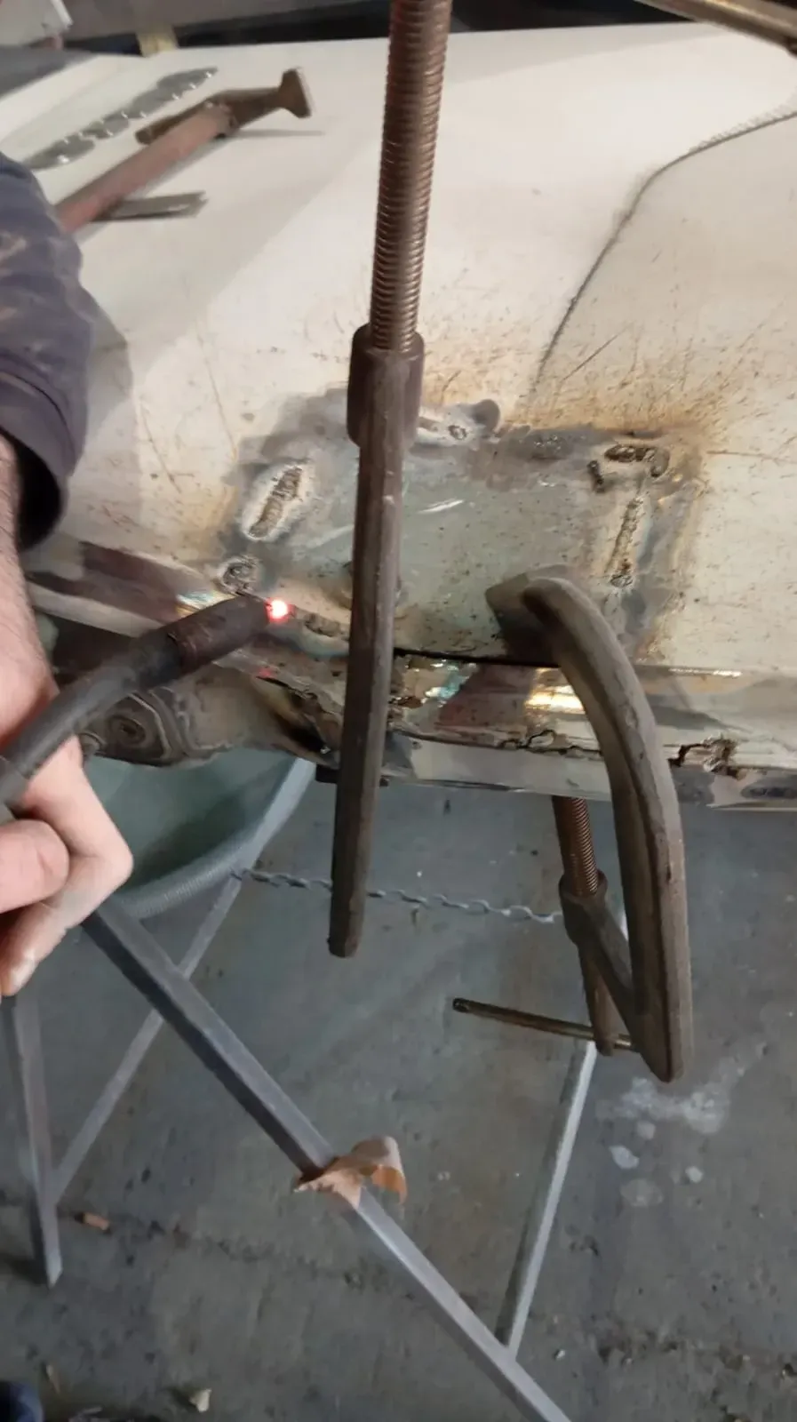 Una persona suelda láminas de metal con una herramienta de soldar, sujetada en su lugar por abrazaderas, utilizando una mesa portátil.