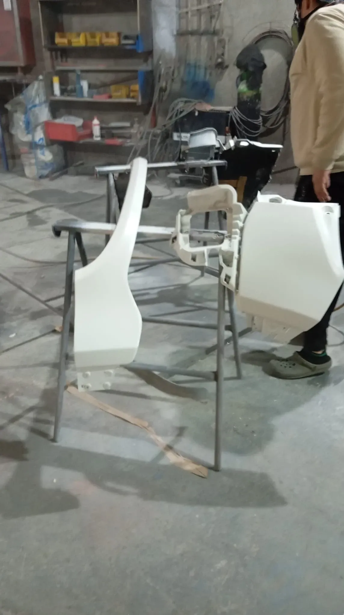 Piezas de automóvil preparadas y listas para pintar, colocadas sobre soportes en un taller, persona con equipo de protección.
