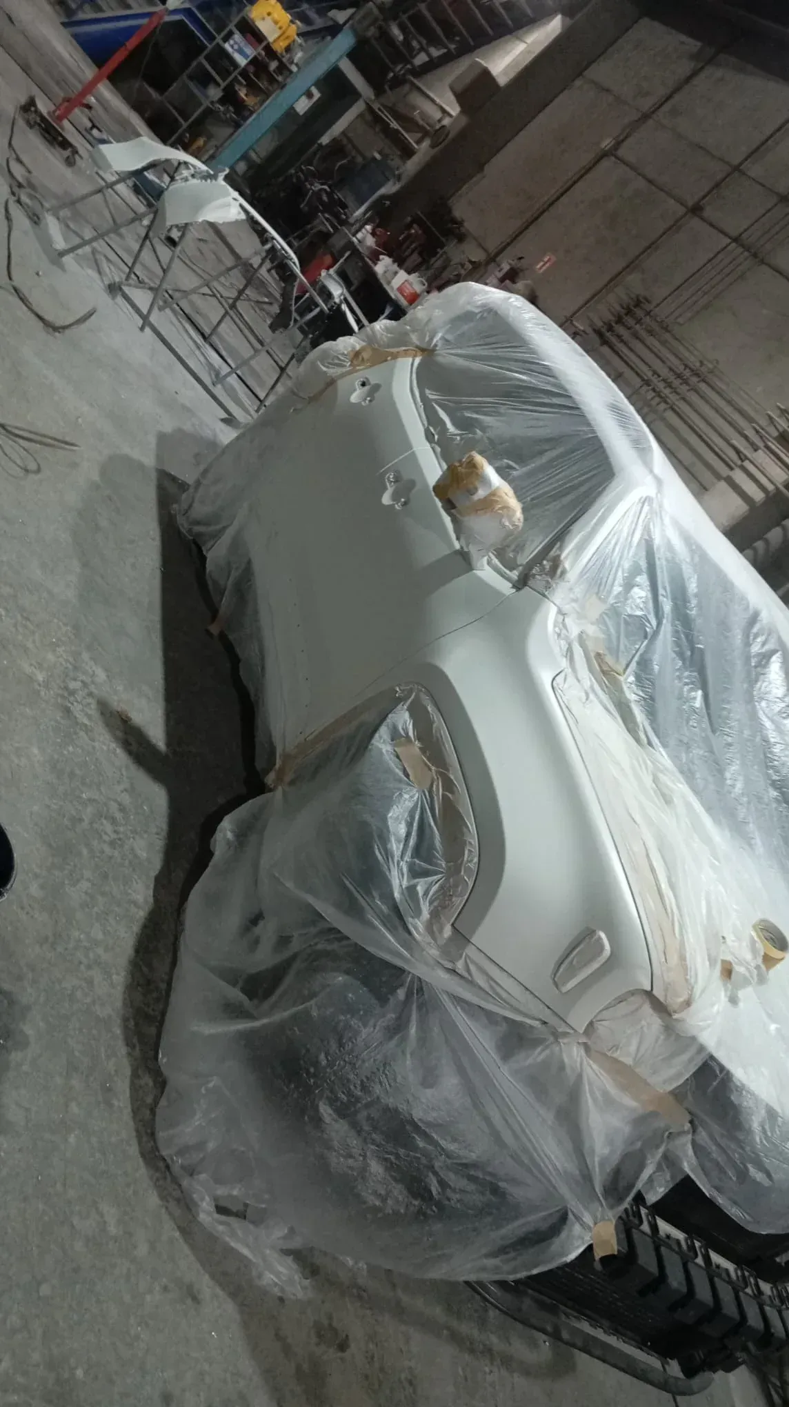 Coche blanco envuelto en plástico en un taller, posiblemente a la espera de reparación o pintura.