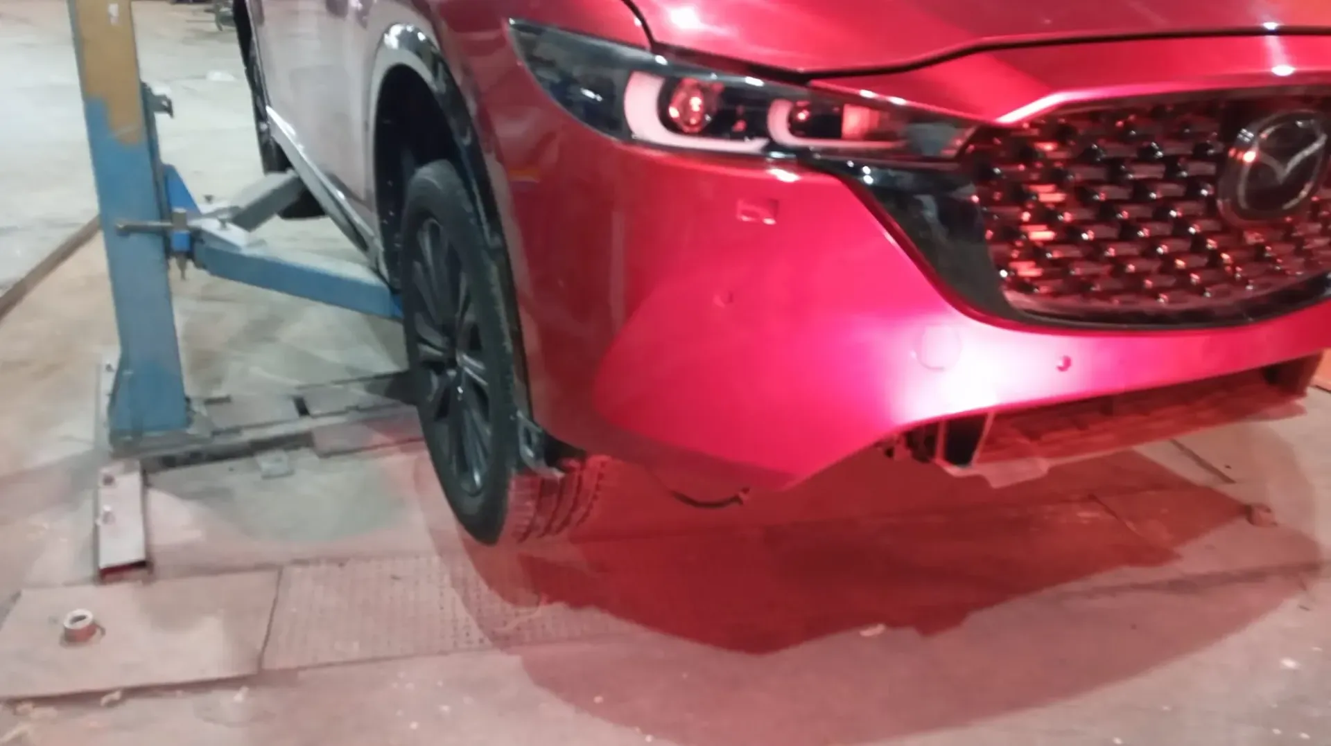 Mazda CX-5 rojo en un elevador de automóviles, parachoques delantero parcialmente removido.