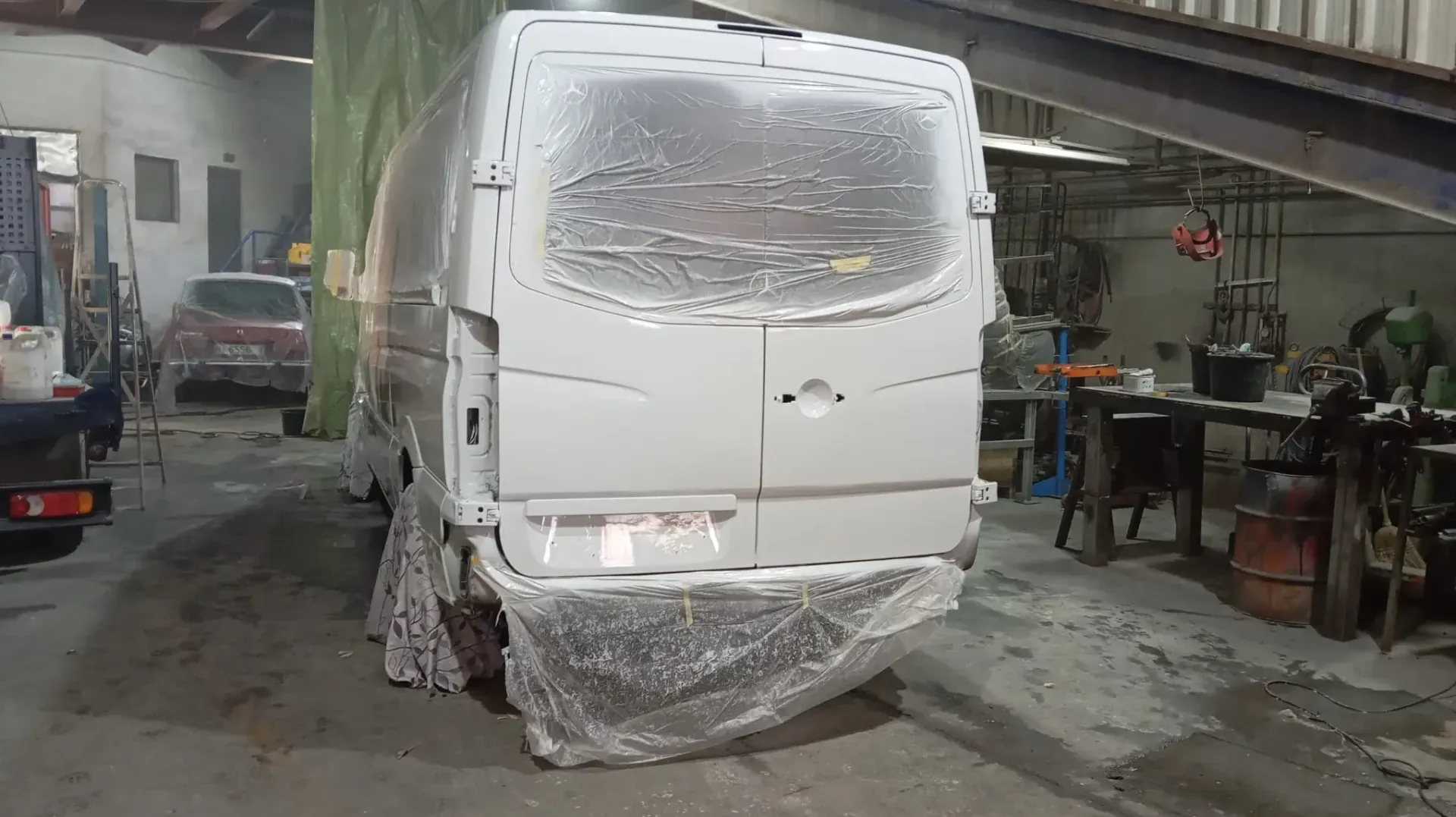 Furgoneta blanca cubierta con plástico en el interior de un taller, probablemente para pintar.