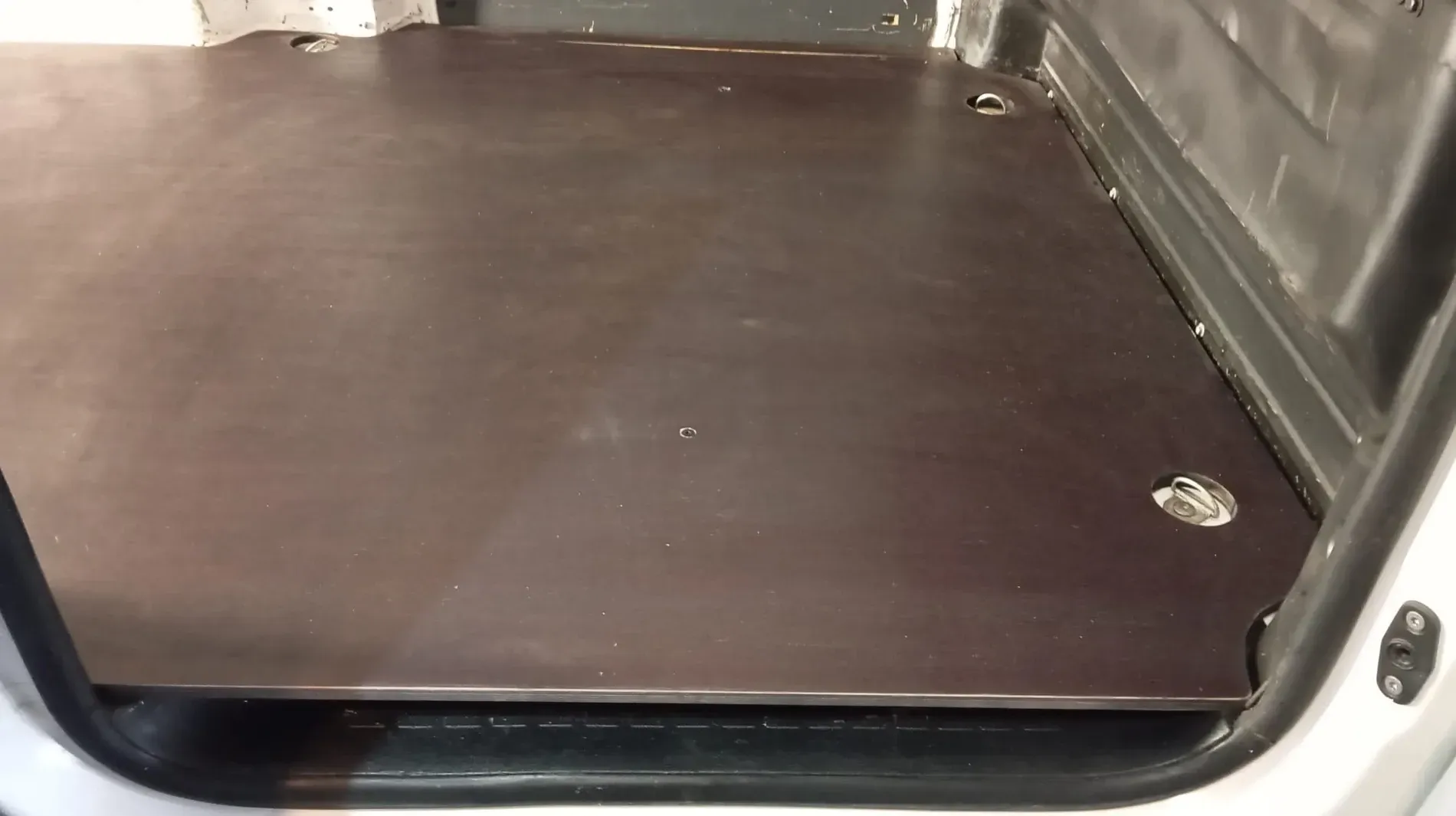 Piso de madera contrachapada marrón instalado en la parte trasera de una camioneta plateada.