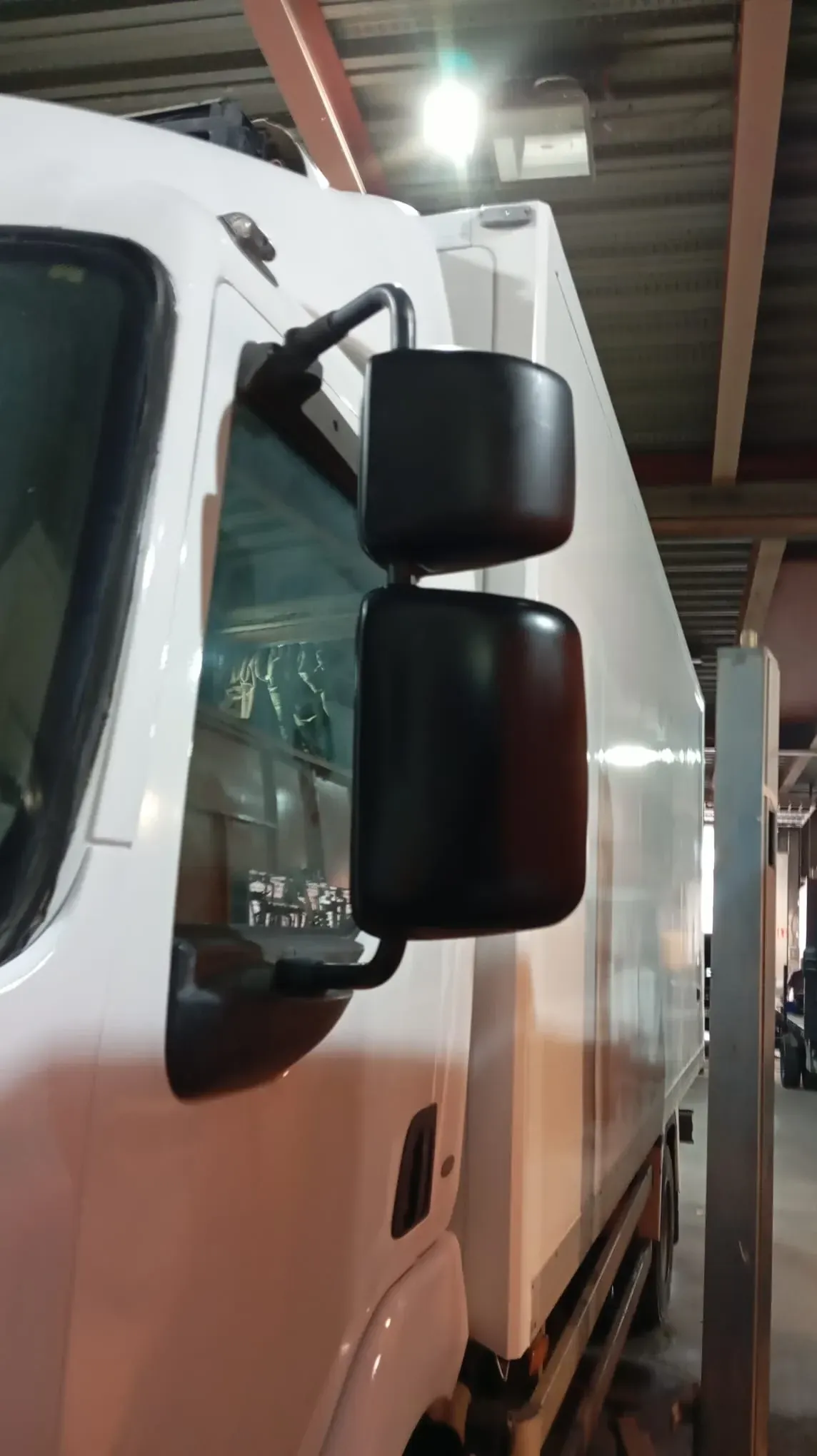 Lateral de camión blanco con espejos laterales dobles negros en un entorno interior.