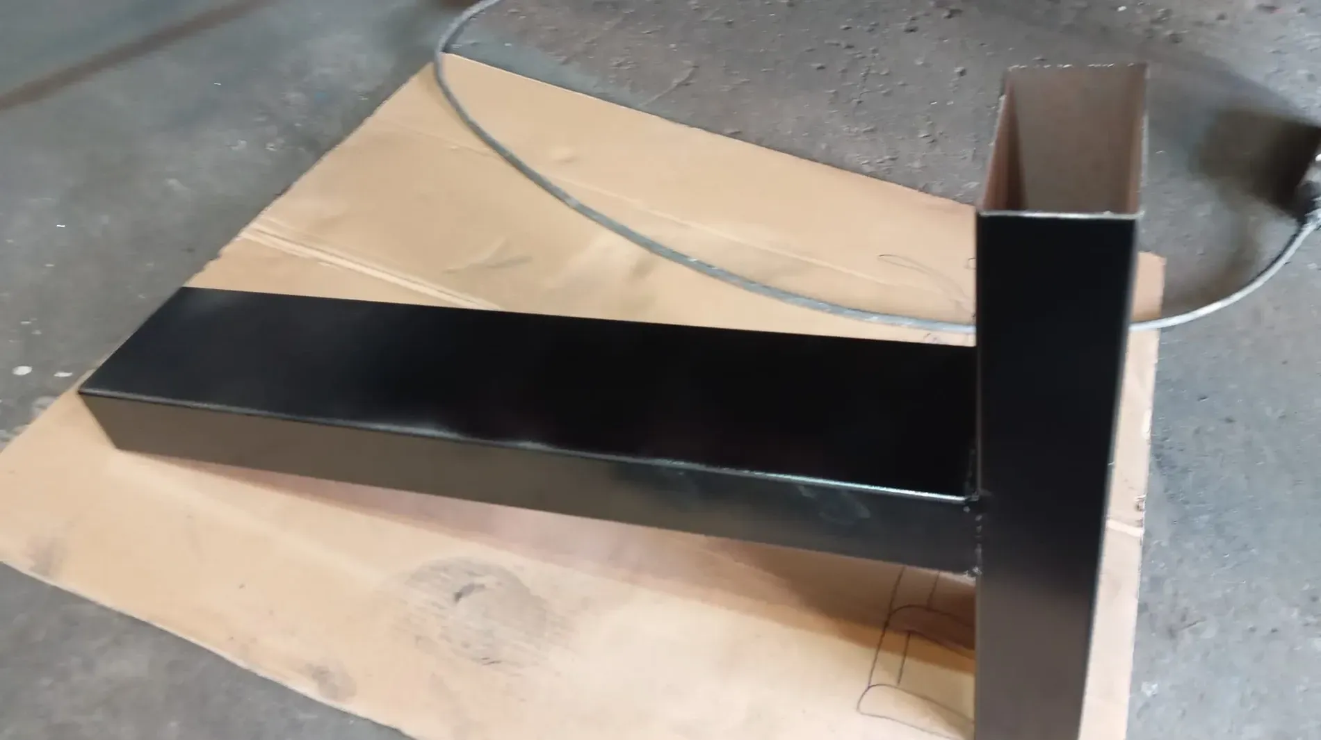 Estructura rectangular de metal negro y poste sobre cartón, probablemente recién pintado.