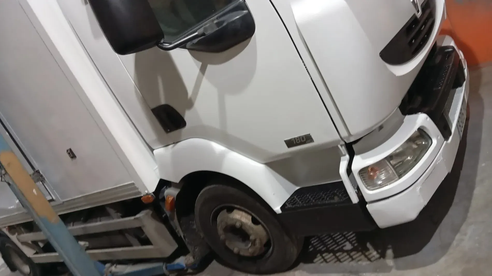 Camión de reparto blanco, vista parcial que muestra la cabina y el lateral, estacionado en el interior, toma en ángulo.