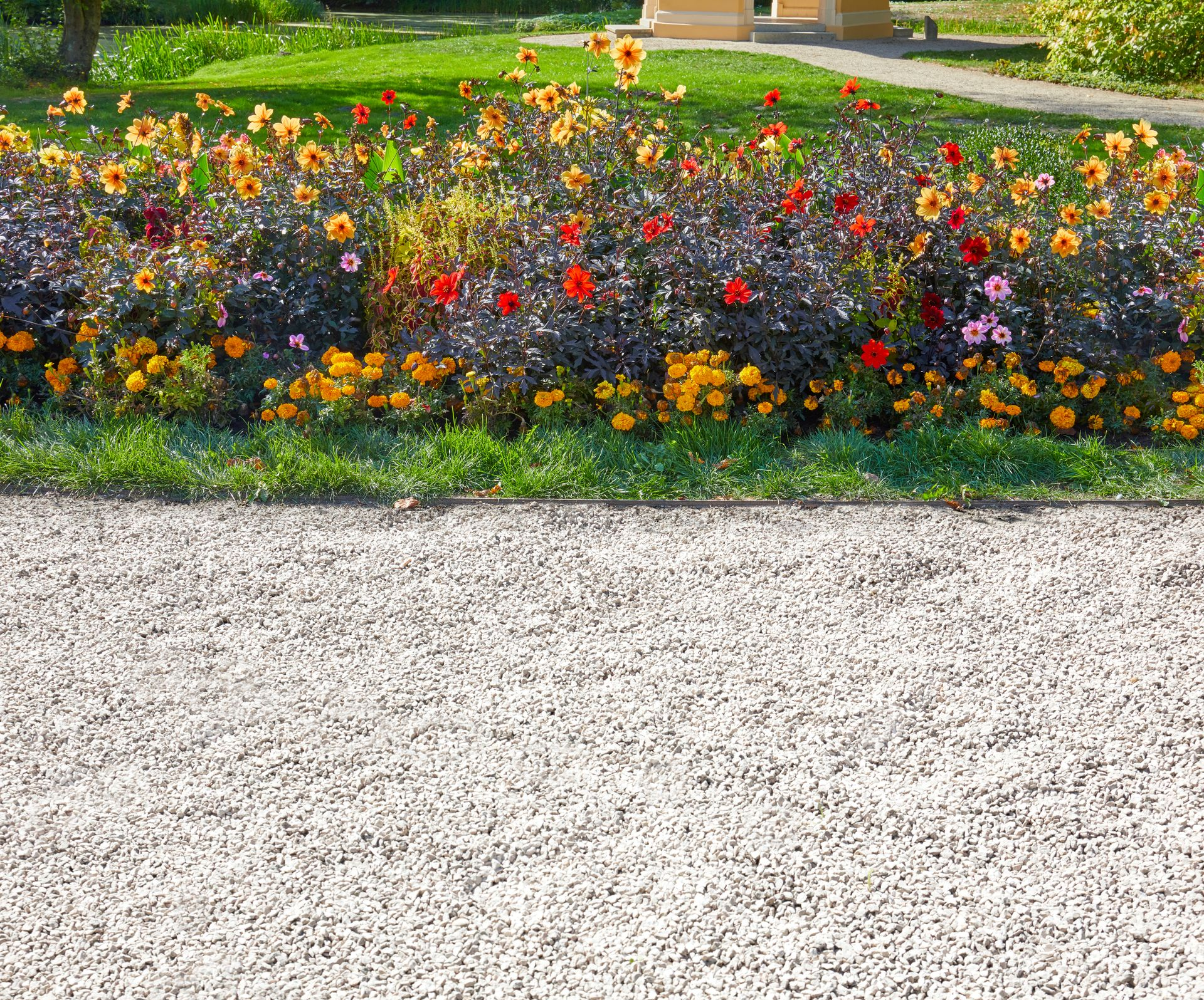 Un parterre de fleurs colorées, devant une pelouse et un chemin de gravier.