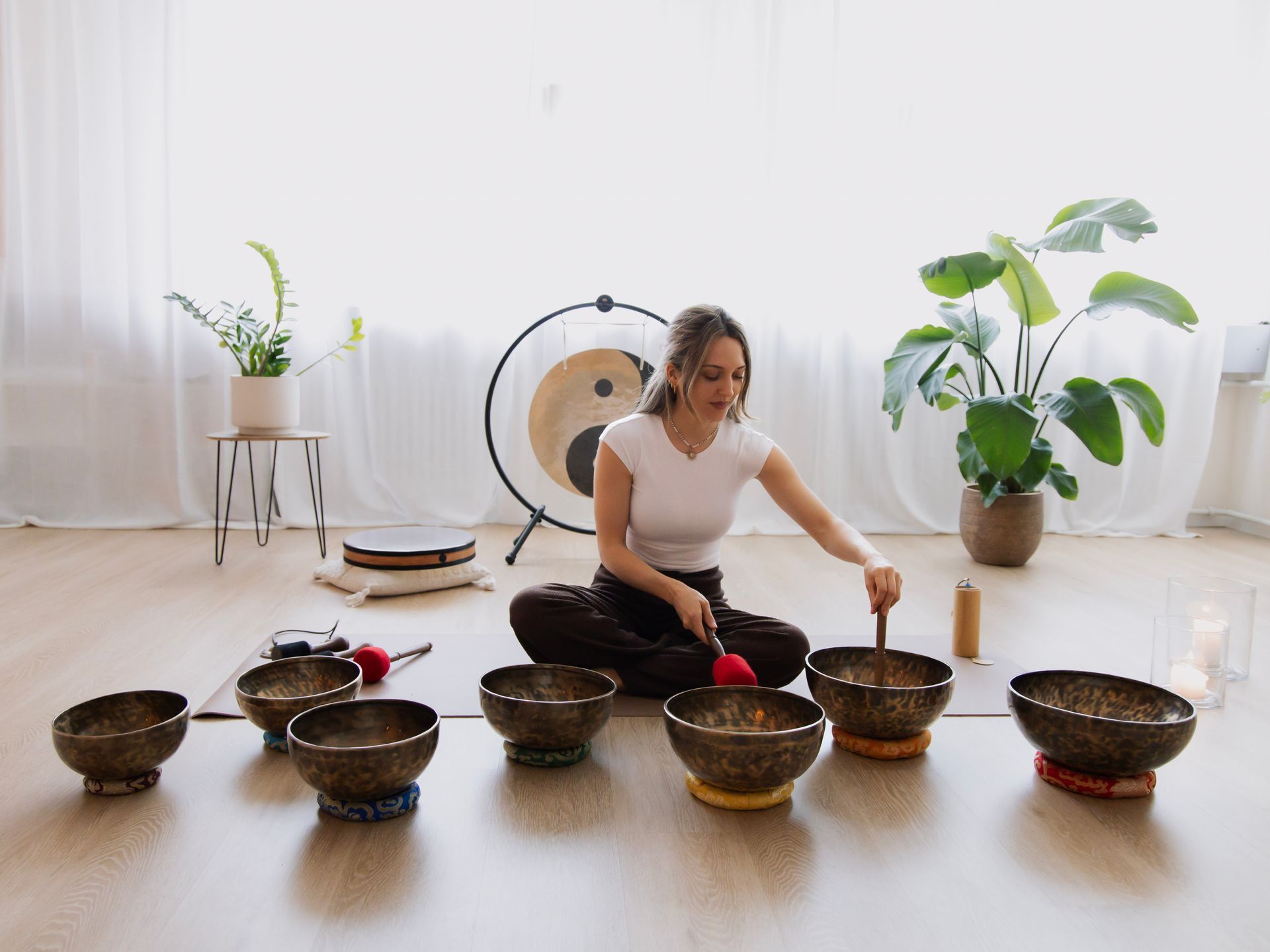 Eine Frau sitzt im Schneidersitz auf einer Yogamatte und meditiert in einem hellen Studio mit weissen Vorhängen.