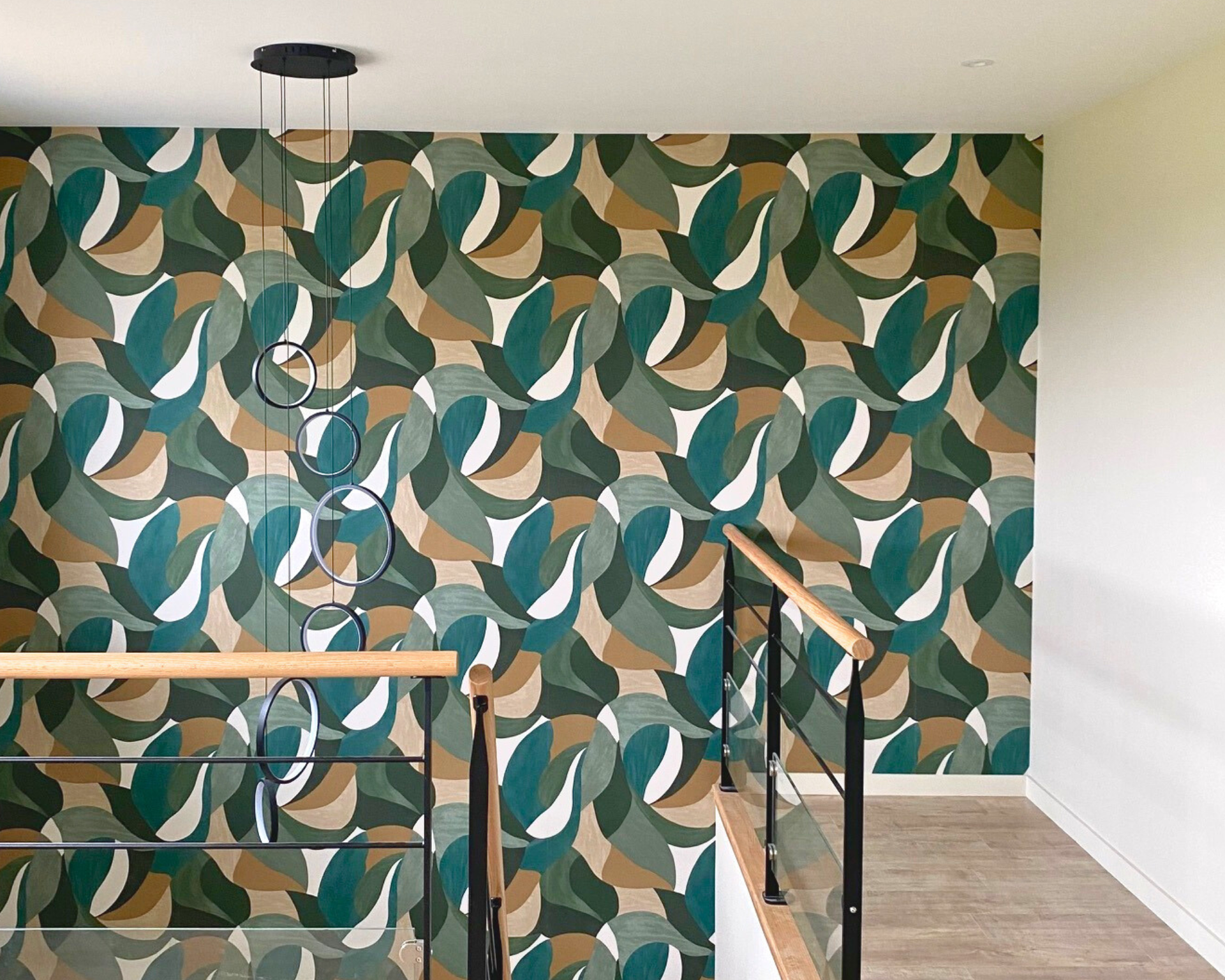 Palier d'escalier avec papier peint à motifs de feuilles vertes, turquoise et beiges et une rampe en bois sur la gauche.