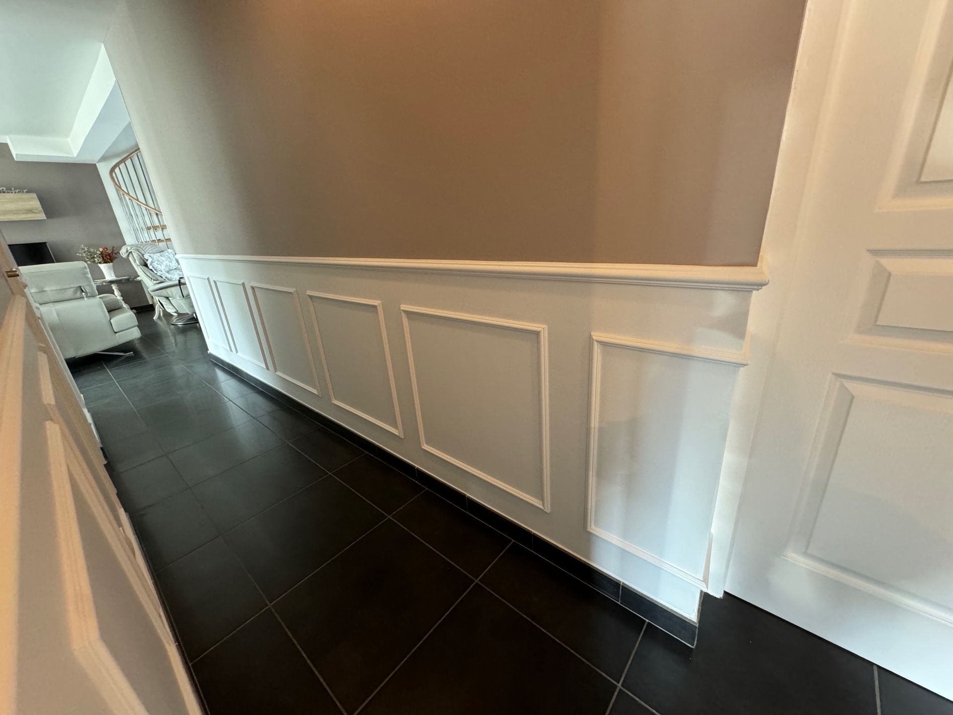 Couloir blanc avec lambris, murs beiges et parquet foncé menant à une pièce.