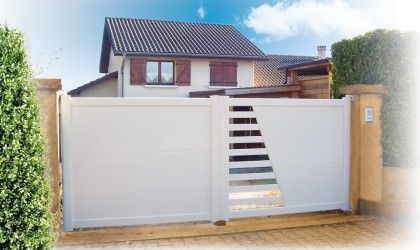 Allée d'entrée avec portail blanc menant à une maison. Conception à claire-voie, avec une fenêtre en diagonale et des piliers en brique.