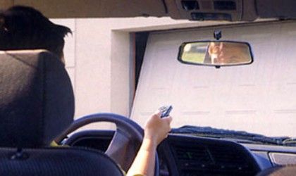 Une personne dans une voiture utilise une télécommande pour ouvrir une porte de garage ; vue de l'intérieur de la voiture.