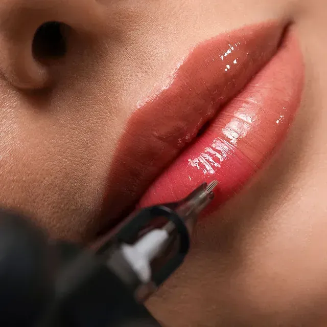 Un primer plano de los labios de una mujer siendo tatuados con una máquina.