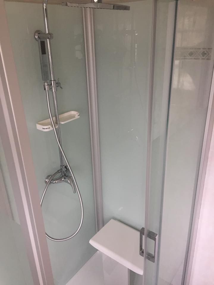 Cabine de douche avec siège, pommeau de douche et portes coulissantes en verre.