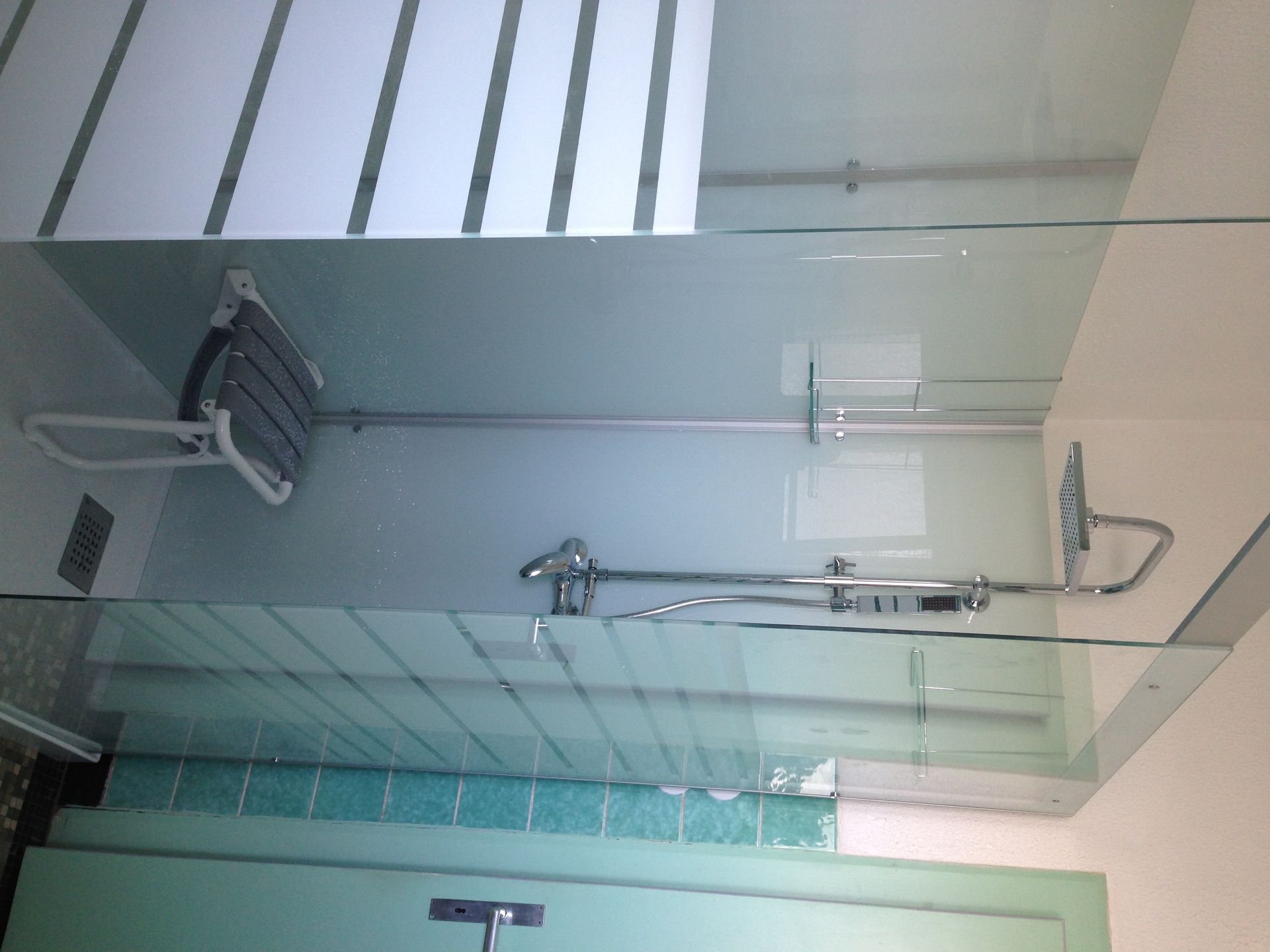 Cabine de douche avec parois en verre, siège rabattable et pommeau de douche. Les parois ont un aspect dépoli.