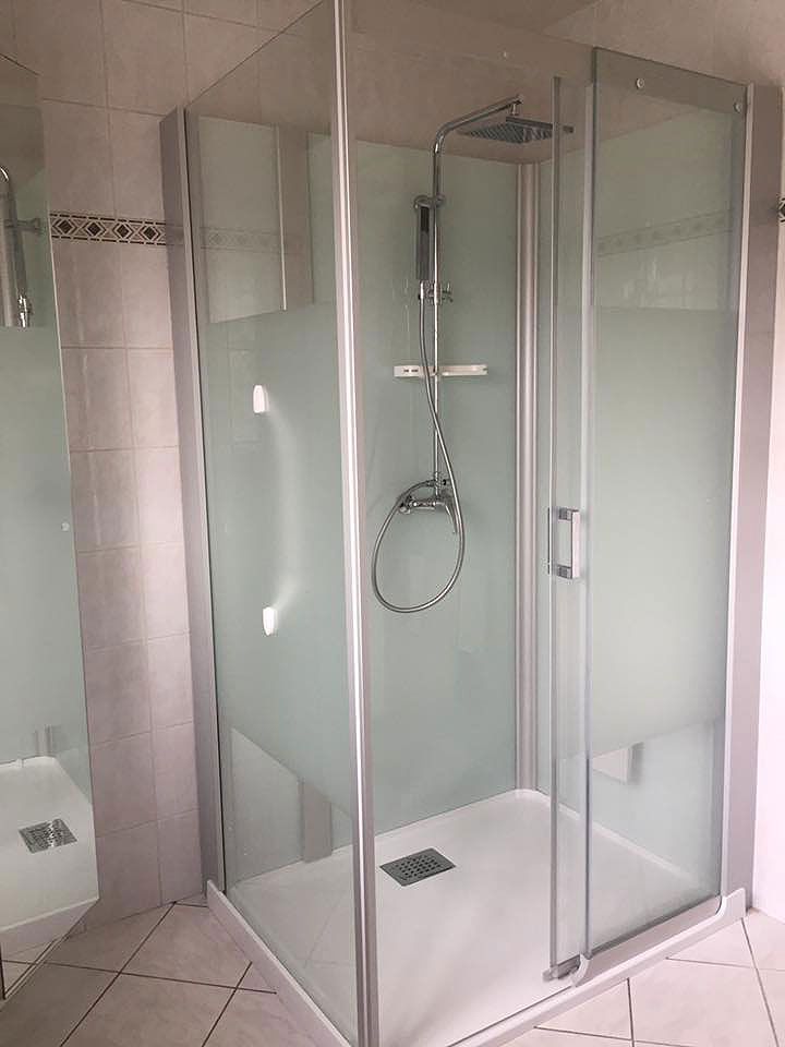 Cabine de douche avec portes en verre dépoli et receveur blanc, dans une salle de bains carrelée.