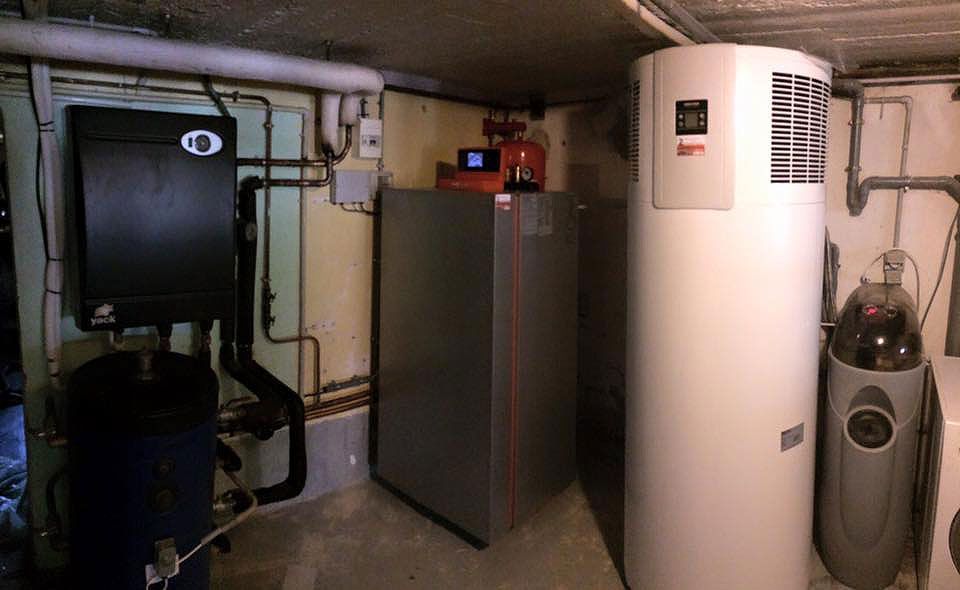 Sous-sol avec les composants du système de chauffage, notamment un boîtier noir, une armoire grise et un réservoir blanc.