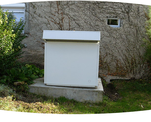 Structure rectangulaire blanche sur une base en béton, adossée à un mur recouvert de vigne, à côté d'une fenêtre et de verdure.