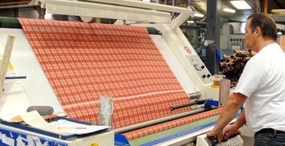 Un homme manipule une machine d'inspection textile, examinant un tissu à motifs rouges et blancs. Environnement d'usine.