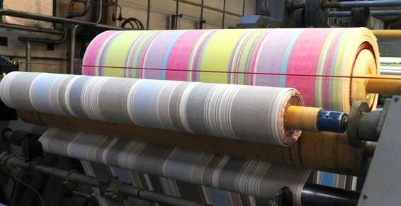 Deux grands rouleaux de tissu rayé sur une machine, l'un rose/jaune, l'autre gris/blanc.