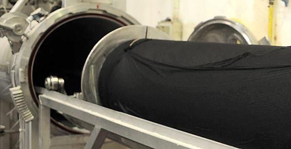 Un grand rouleau de tissu noir est chargé dans une machine industrielle cylindrique, probablement pour la teinture.