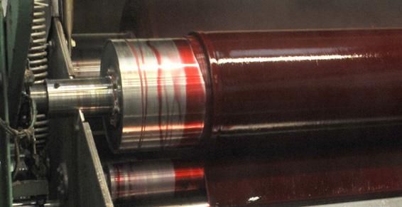 Rouleau industriel recouvert d'encre dans une machine, avec engrenages et composants métalliques visibles.