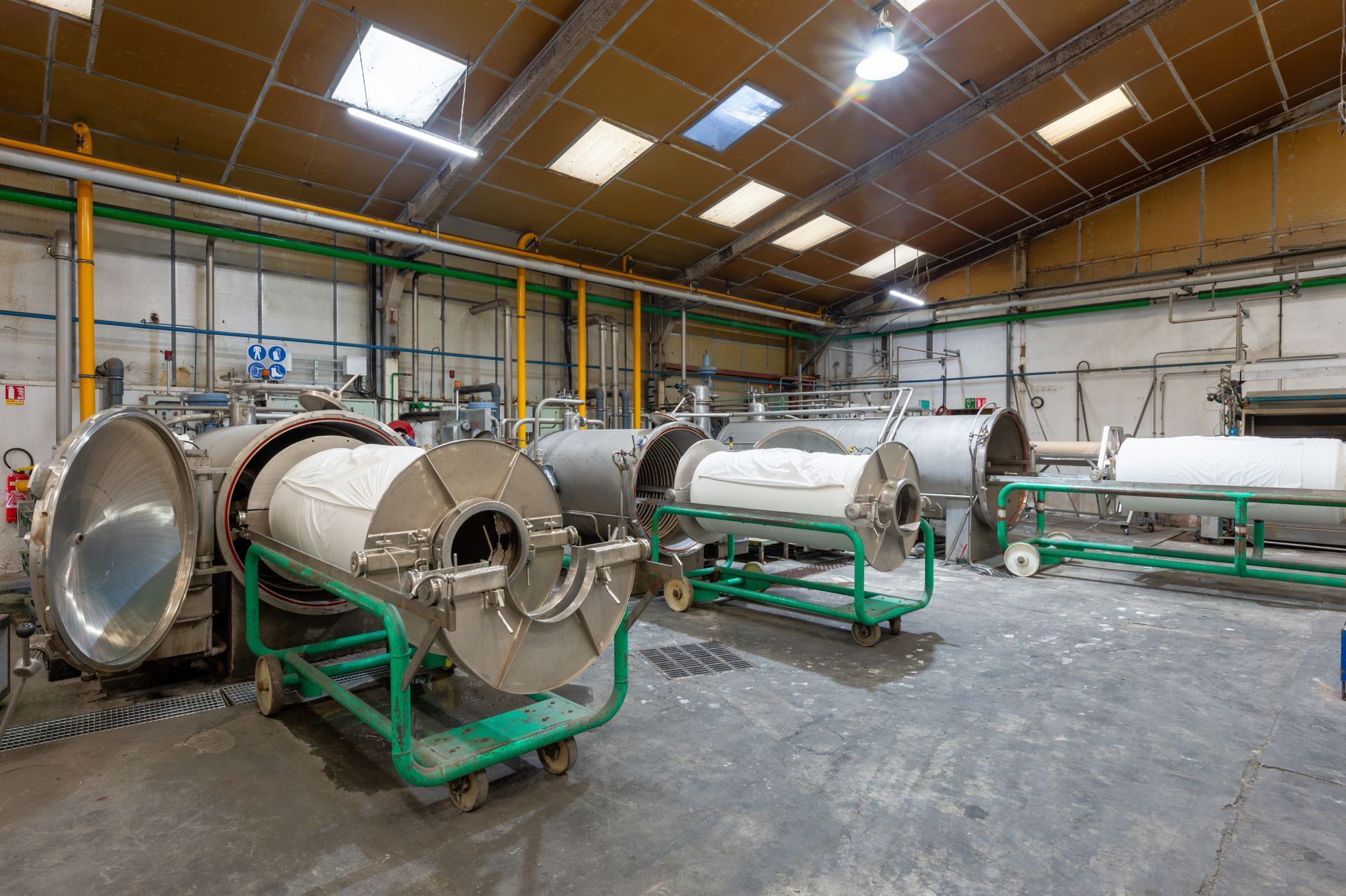 Intérieur d'une installation industrielle avec de grandes machines cylindriques sur des chariots à roues vertes.
