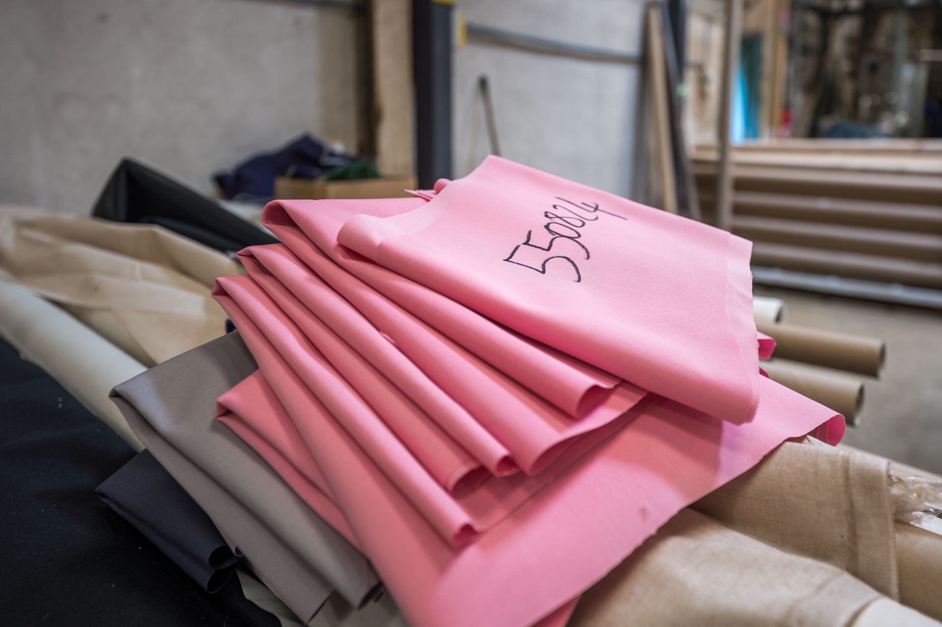 Du tissu rose empilé sur d'autres rouleaux de tissu dans un atelier.