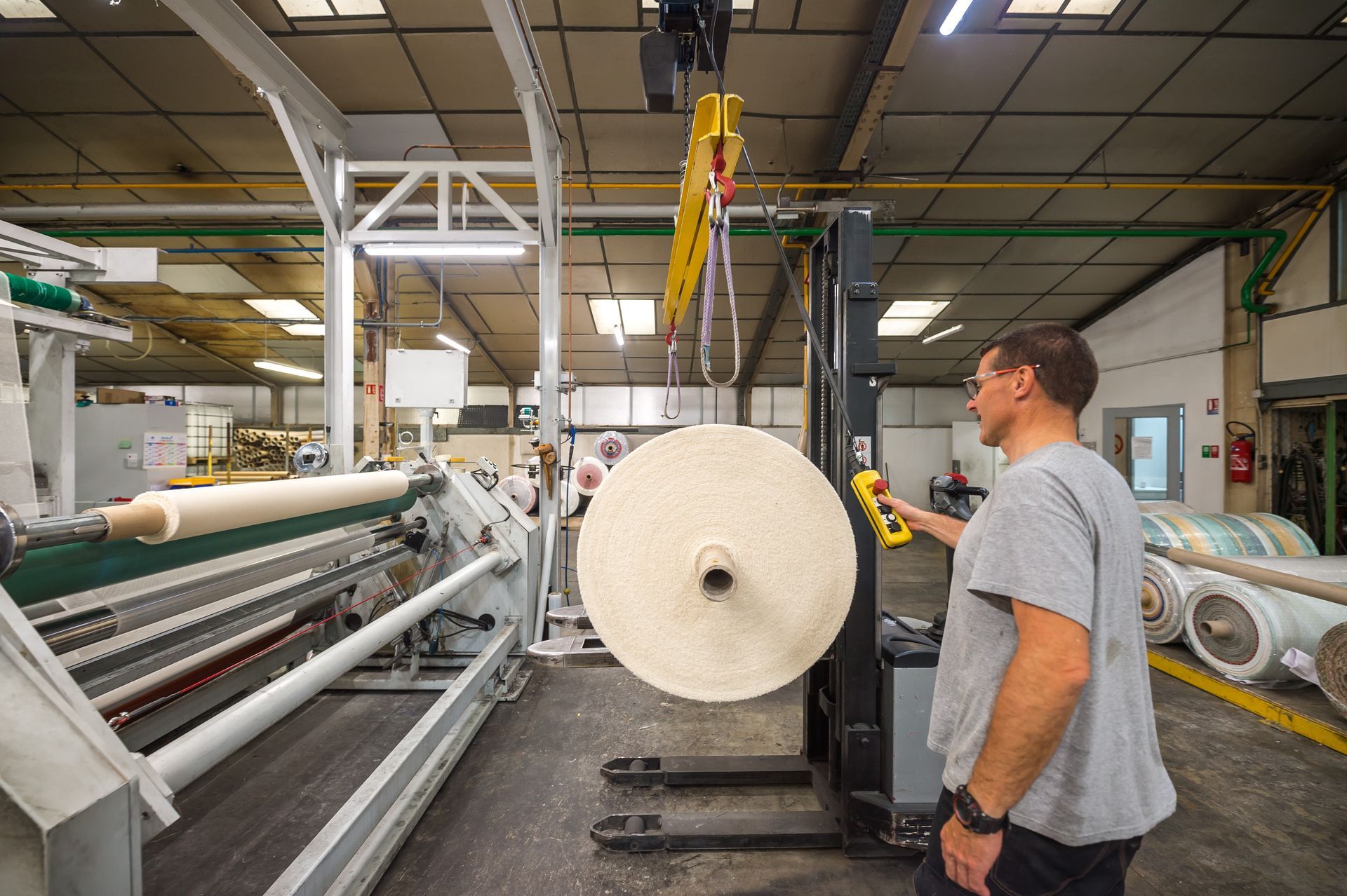 Un homme manœuvre un chariot élévateur dans une usine, soulevant un gros rouleau de papier.