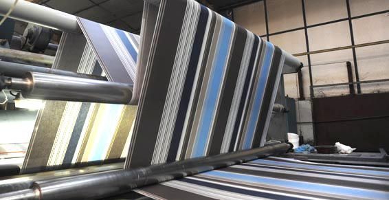 Tissu rayé traité sur des rouleaux industriels dans une usine.