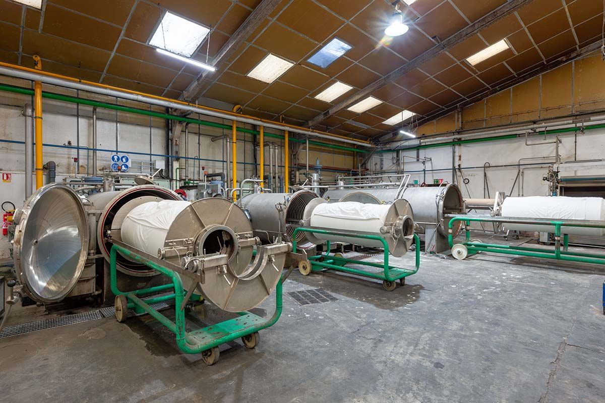 De grands cylindres industriels à l'intérieur d'une usine. Des réservoirs métalliques sur des châssis à roues, sous une verrière.