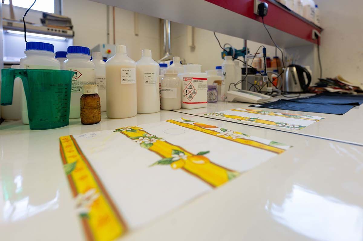 Espace de travail du laboratoire : flacons, verre doseur et impressions sur une surface blanche avec une fenêtre et une étagère rouge.