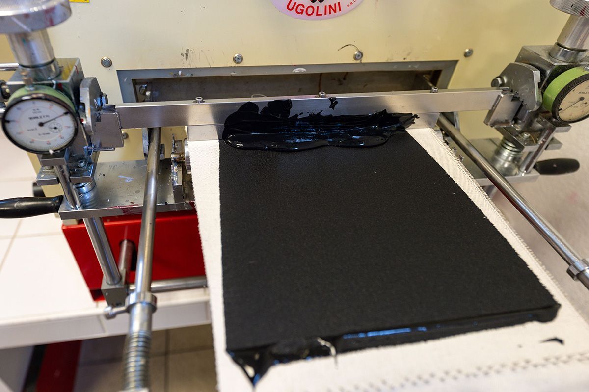 Une substance noire et visqueuse est étalée sur un plateau par un dispositif mécanique, en laboratoire.