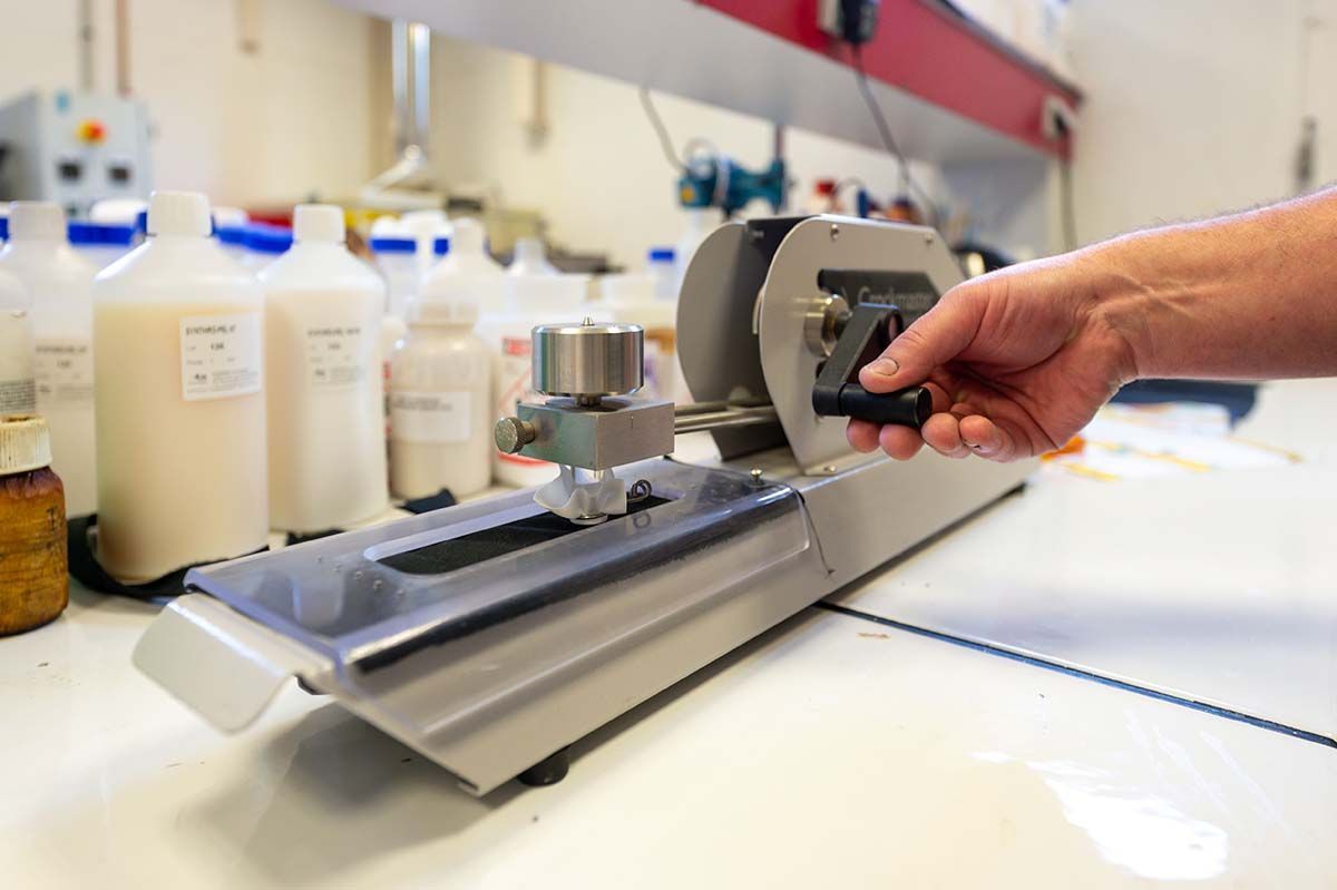 Main utilisant un appareil dans un environnement de laboratoire avec des flacons blancs et un plan de travail de couleur claire.