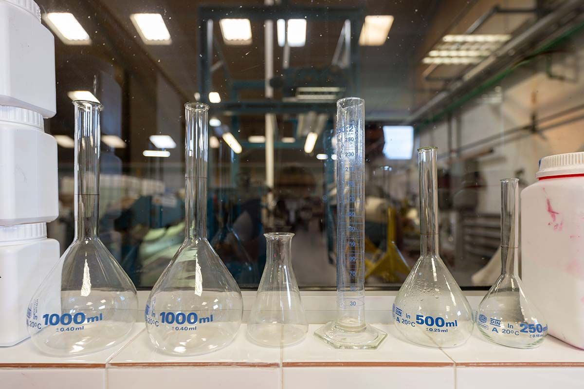 Béchers et éprouvettes graduées en verre posés sur une paillasse de laboratoire, se reflétant dans une fenêtre.