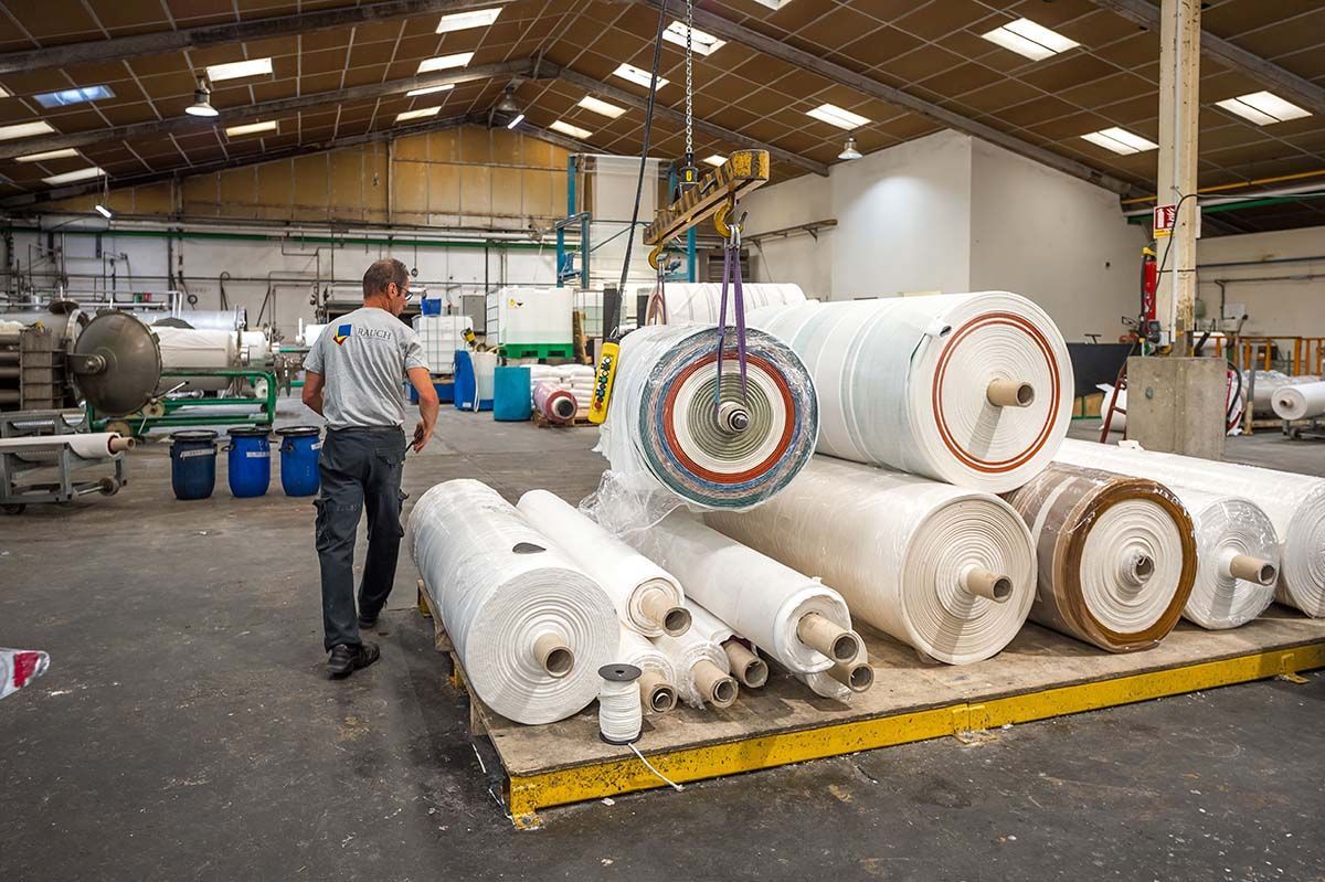 Un homme marche près de rouleaux de matériau empilés dans un entrepôt. Pont roulant.