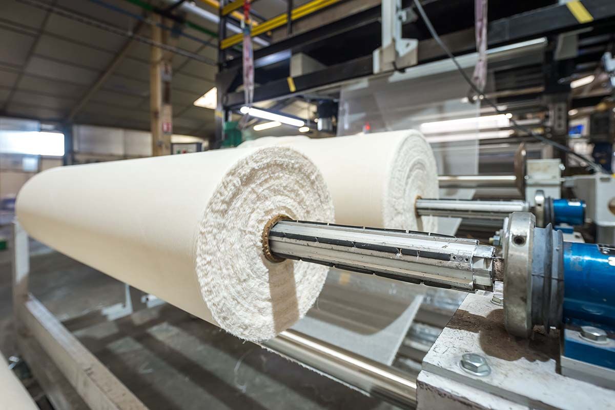 Rouleaux de tissu beige sur des machines industrielles dans une usine.