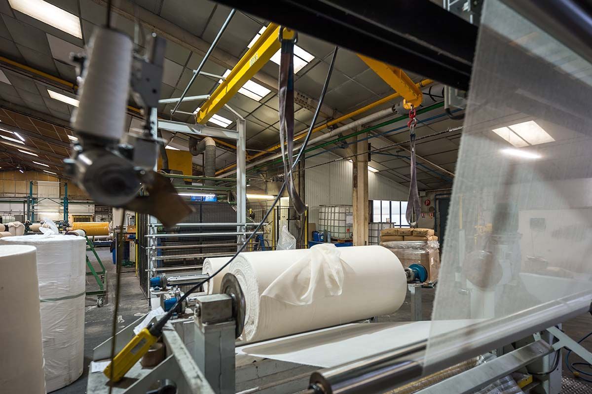 Machines d'usine produisant de grands rouleaux de tissu blanc.