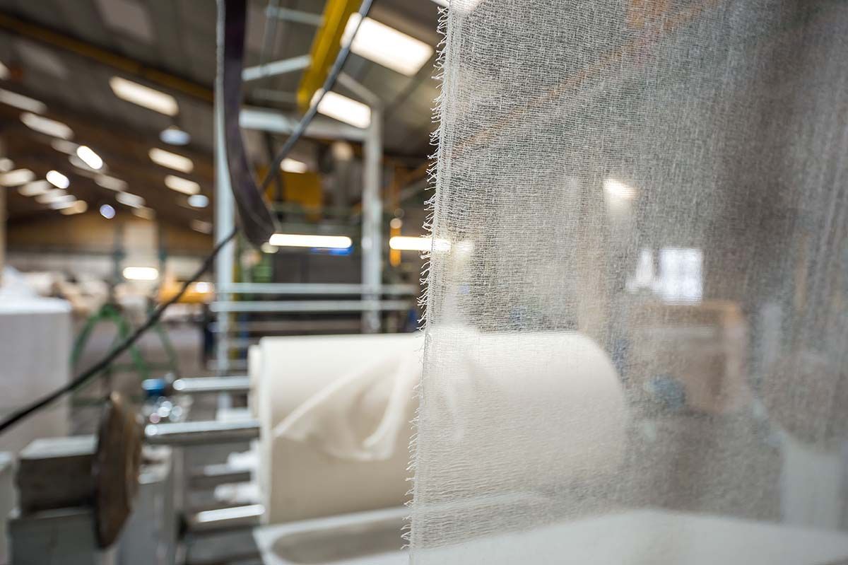 Découpe d'une feuille de plastique transparent dans un environnement industriel, avec des rouleaux de matériau blanc en arrière-plan.