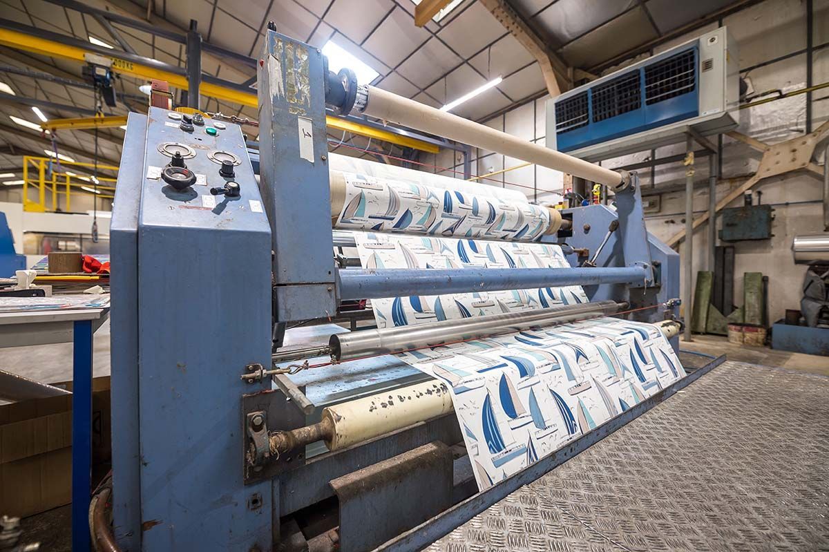 Machine d'impression textile dans une usine, imprimant des motifs nautiques bleus et blancs sur des rouleaux de tissu.