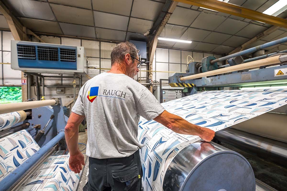 Un homme actionne une machine d'impression textile dans une usine. Rouleau de tissu à motifs bleus et blancs.
