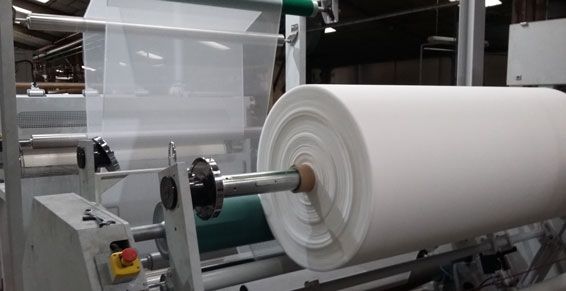 Grand rouleau de matériau blanc sur une machine industrielle, avec une feuille translucide en arrière-plan.
