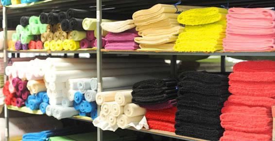 Des étagères remplies de textiles colorés soigneusement empilés, notamment des serviettes et des rouleaux de tissu.