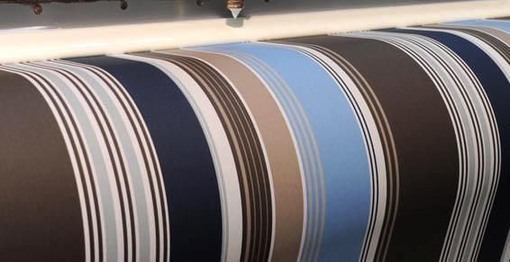 Fabrication d'un grand rouleau de tissu à rayures bleues, brunes, grises et blanches.