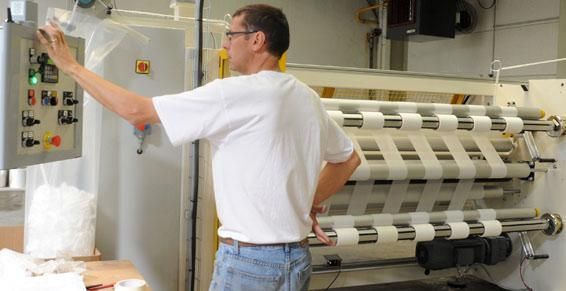 Un homme manipule une machine dans une usine. Il touche un panneau de commande tout en observant l'équipement.