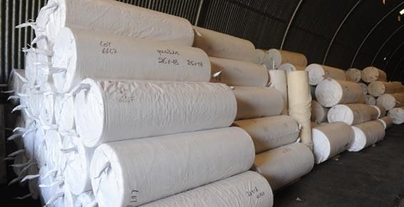 De grands rouleaux de tissu blanc sont empilés dans un entrepôt.