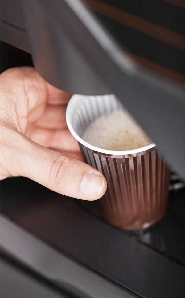 Una persona está vertiendo una taza de café en una máquina de café.